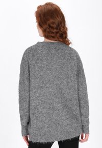 Grauer Strickpullover mit lockerer Passform, der eine flauschige Textur, lange Ärmel, einen runden Ausschnitt und einen längeren hinteren Saum aufweist.