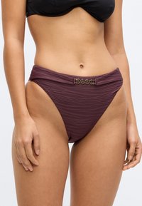 Donker bordeauxrode bikinibroek met een gestructureerd ontwerp en een gedraaide tailleband. Voorzien van goudkleurige accenten aan de voorkant met de merknaam.