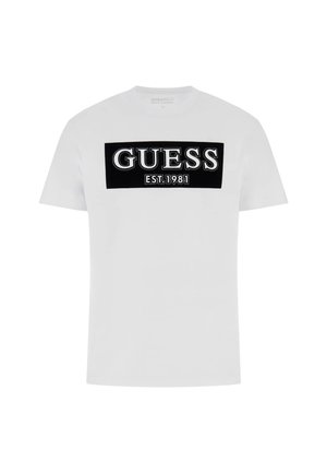 T-shirt bianco in cotone con una grafica rettangolare nera con la scritta "GUESS" e "EST. 1981" in bianco. Maniche corte, scollatura a girocollo.