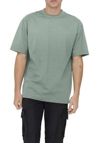 Short-sleeve t-shirt in light green cotton, featuring a round neckline and a relaxed fit, paired with black cargo pants.