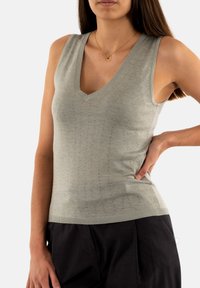Top sin mangas de color gris claro con escote en V, que presenta un patrón de punto texturizado y pequeños detalles reflectantes. Tejido suave con un diseño ajustado.