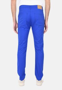 Pantaloni in cotone blu con una vestibilità slim, dotati di tasche posteriori e una patch in pelle marrone chiaro sulla cintura. Texture liscia e design sartoriale.