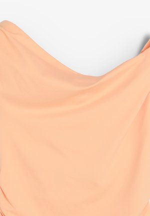 Dos manos sosteniendo y estirando una gran tela de color durazno contra un fondo blanco.