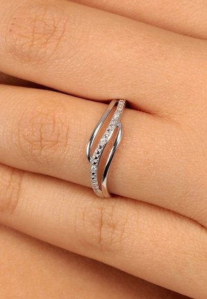 Silberner Ring mit Wellenmuster, der eine Reihe von kleinen Diamanten aufweist und an einem Finger auf heller Haut getragen wird.