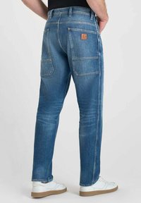 Jeans in denim di un blu chiaro con una vestibilità slim, dotati di due tasche posteriori e di una patch in pelle con il logo sulla cintura.