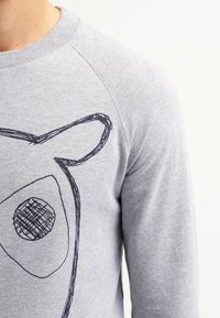 Jasnoszara bluza z dużym czarnym szkicowanym wizerunkiem zwierzęcej twarzy na przodzie, z okrągłym nosem i spiczastymi uszami.