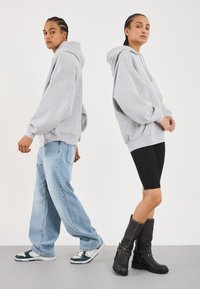 Felpe grigie oversize indossate da modelli maschili e femminili. Modello maschile abbinato a jeans larghi azzurri e sneakers; femminile in pantaloni bike neri e stivali al ginocchio.