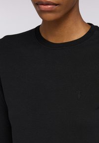 Felpa nera con collo rotondo e finiture a costine. Presenta un piccolo logo ricamato sul petto dello stesso colore. Texture liscia.