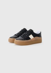 Svarta sneakers med en strukturerad design, med en vit rand, svarta snören och en beige gummisula. Mjuk innersula.