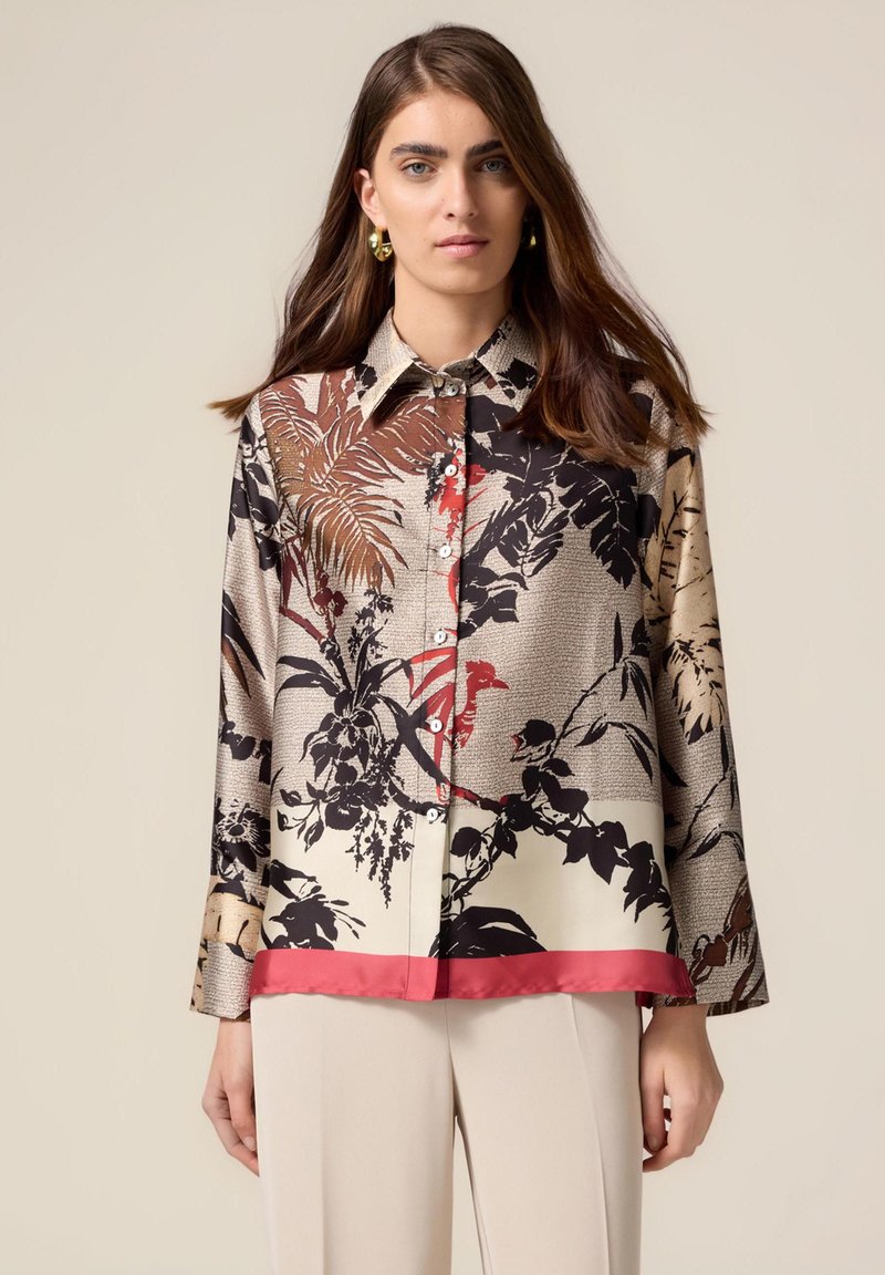 Blusa di seta con stampa floreale in nero, marrone e rosso, con orlo rosso a contrasto e chiusura con bottoni. Maniche lunghe e design con colletto.