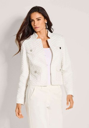 Witte gewatteerde jas met kraag, voorzien van vier zakken en zilverkleurig beslag. Draagt over een wit shirt en gecombineerd met lichtgekleurde broek.