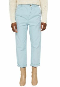 Pantalon bleu clair à taille haute avec ourlet retroussé, fermeture à boutons sur le devant et poches latérales, associé à des bottines beige.