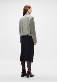 Γκρίζα πλεκτή μπλούζα, μαύρη μίντι φούστα και γυαλιστερές καφέ μπότες μέχρι το γόνατο. Η μπλούζα έχει ψηλό γιακά και χαλαρή εφαρμογή; οι μπότες διαθέτουν υφή.