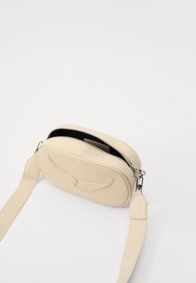 Cream leather crossbody bag with a rounded shape, zipper closure, and embossed wing design on the front. Adjustable fabric strap attached.