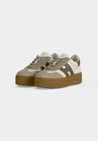 Ζευγάρι πλατφόρμα sneakers με μπεζ σουέντ, λευκό δέρμα, σκούρες πράσινες λεπτομέρειες και χοντρές καφέ λαστιχένιες σόλες, από μπροστινή αριστερή γωνία.