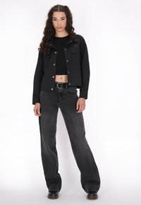 Sort cropped jakke med knaplukning foran og to brystlommer, parret med højtaljede, løse sorte denimjeans og sorte sko.