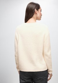 Helles beigefarbenes, flauschiges Sweatshirt mit lockerer Passform, rundem Ausschnitt und langen Ärmeln. Der Stoff wirkt weich, hat minimale Nähte und eine strukturierte Oberfläche.