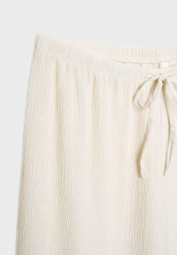 Ljust beige texturerade byxor med en skrynklig tygdesign, elastisk midja och en diskret knytning.