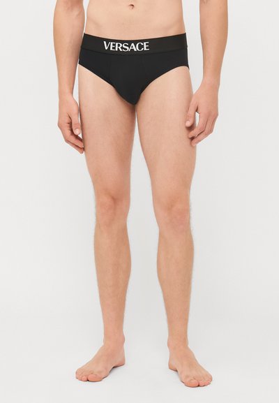 Boxers noirs pour hommes avec une ceinture en logo "VERSACE" blanche, fabriqués en tissu lisse avec un ajustement serré, conçus pour le confort et le soutien.