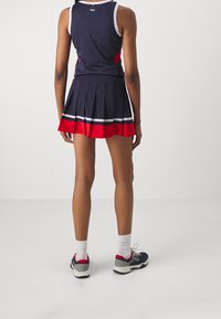 Marinblå ärmlös topp med röda detaljer, kombinerad med en röd- och marinblå plisserad kjol med vita ränder. Bärs med marinblå sportskor och vita strumpor.