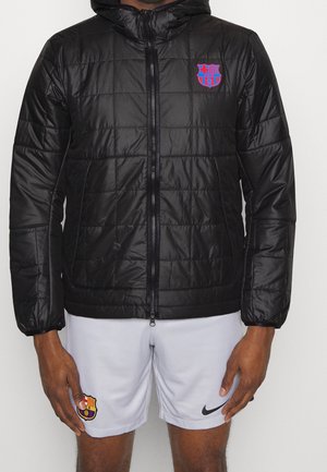 Mies, joka pukeutunut mustaan tikattuun huppariin, jossa on FC Barcelonan logo, ja valkoisiin Nike-urheilushortseihin, joissa on FC Barcelonan vaakuna.