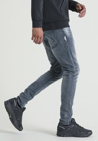 Gray denim jeans with a slim fit, featuring back pockets, and complemented by black athletic sneakers with textured detailing.