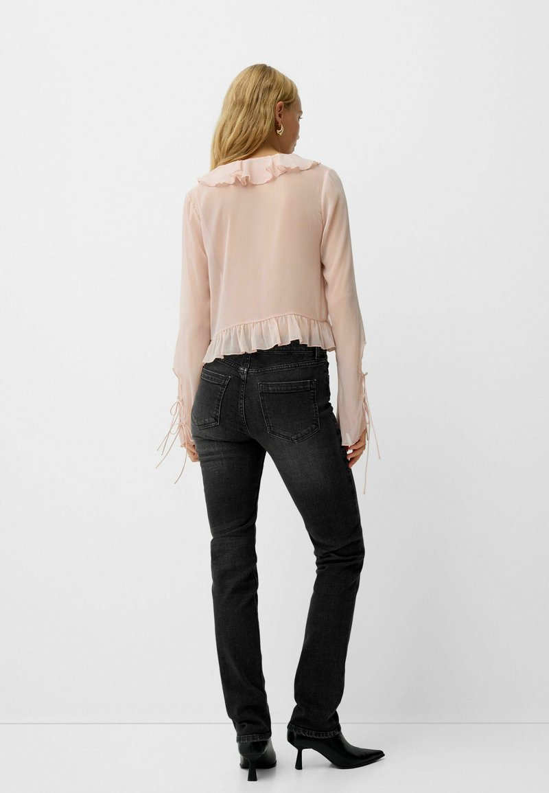 Blusa rosa trasparente con colletto e orlo arricciati, abbinata a jeans neri attillati e tacchi neri a punta. Maniche lunghe con polsini legati.