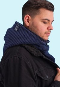 Knitted navy scarf with ribbed texture and a tag, paired with a dark black jacket featuring a fuzzy collar.