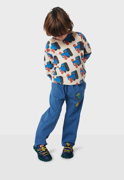 Sudadera de algodón con patrones gráficos caprichosos en azul, rojo y negro; pantalones de mezclilla azul con bordado de dados juguetones; zapatillas negras y amarillas.