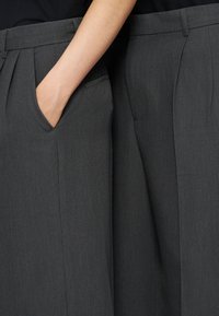 Gros plan de deux personnes portant un pantalon gris foncé, dont l'une a la main placée dans la poche avant.