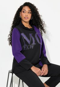 Svart och lila sweatshirt med en huva, 3/4 ärmar och dekorerad text "M O VIEW" i rhinestones. Mjuk tygkvalitet, avslappnad passform.