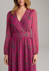 Fuchsiefarbenes Wickelkleid mit langen, transparenten Ärmeln, das mit einem Schwarz-Pink-Wellenmuster, strukturiertem Stoff und einer taillierten Passform versehen ist.