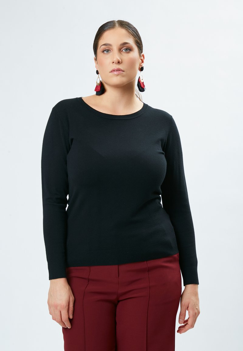 Maglione nero a maniche lunghe con scollatura tonda, polsini a coste e una consistenza liscia, abbinato a pantaloni eleganti bordeaux.