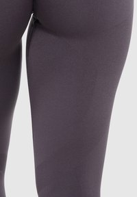 Leggings a vita alta di colore grigio scuro con tessuto testurizzato, caratterizzati da una superficie liscia e sottili elementi di design curvi lungo i lati.