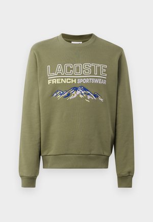 Olive green sweatshirt with long sleeves, crew neck, featuring "LACOSTE FRENCH SPORTSWEAR" text and an embroidered mountain design in blue.