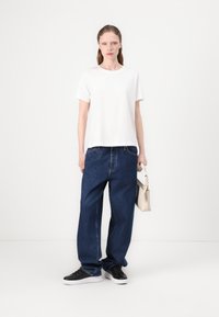 Witte katoenen t-shirt, losse blauwe spijkerbroek, zwarte sneakers en een lichtgekleurde handtas. Eenvoudig, casual ontwerp met een rechte pasvorm.