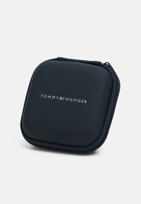 Crna torbica sa zatvaračem marke Tommy Hilfiger. Ima glatku vanjsku površinu s zaobljenim rubovima i logotip na prednjoj strani. Tekstura zatvarača kao dodatak.