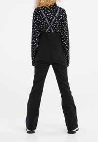 Čierne montérky s nastaviteľnými popruhmi a bielym textom. Dlhý rukáv s vzorom, hladká textúra a rozšírený strih nohavíc.