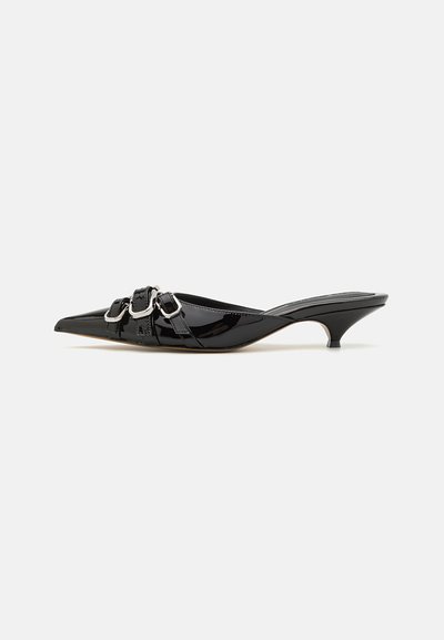 Mules de charol negro con punta afilada, que presentan dos hebillas metálicas y un tacón pequeño. Textura suave y diseño elegante.