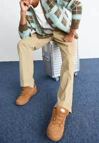 Hnědé tenisky, béžové kalhoty a zeleno-hnědý argyle svetr. Textura je jemná, s vrstveným designem a viditelným šitím.