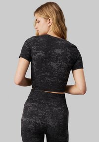 T-shirt nera cropped con maniche corte, caratterizzata da un motivo testurizzato. Il tessuto presenta un design grigio screziato, offrendo una silhouette aderente.