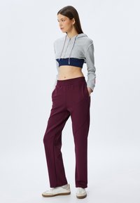 Sudadera gris corta con acentos en azul marino, combinada con pantalones jogger burdeos que tienen bolsillos laterales y un acabado texturizado. Zapatillas blancas completan el look.