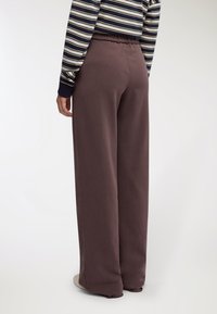 Pantaloni sportivi marroni a gamba larga con vita elastica, realizzati in materiale morbido, mostrati di schiena con una vestibilità comoda e dettagli minimi.