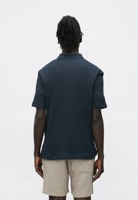 Kortermet polo i mørk marineblå med ribbestruktur og krage. Brukt med lys beige shorts.