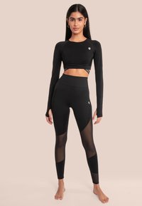 Zwarte sportieve crop top met lange mouwen, voorzien van textuurpanelen en een logo. Hoge taille zwarte leggings met mesh accenten in een strakke design.