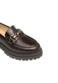 Mocassino in pelle marrone con suola spessa, dotato di una catena decorativa in oro che attraversa il piano del piede e una finitura liscia sulla tomaia.