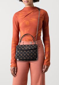Black patterned handbag with a structured design, dual handle and chain strap. Made of textured material featuring a gold emblem, paired with an orange top.