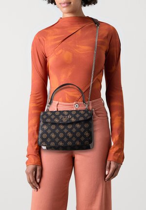 Black patterned handbag with a structured design, dual handle and chain strap. Made of textured material featuring a gold emblem, paired with an orange top.
