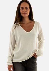Maglione crema a V con maniche lunghe, realizzato in un morbido tessuto testurizzato. Vestibilità rilassata e design semplice senza modelli o accenti visibili.