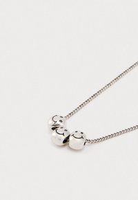 Srebrny naszyjnik łańcuszkowy z trzema okrągłymi koralikami, z których każdy ma czarną buźkę na jednolitym białym tle.